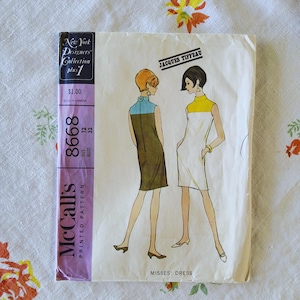 May include: Vintage McCall's printed pattern with a Jacques Tiffeau design for a Misses' dress. The illustration shows two women in mod-style dresses. The pattern includes the text "New York Designers Collection plus 1" and "8668".