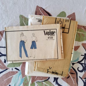 May include: A collection of vintage Vogue sewing patterns. The primary pattern features illustrations of a woman in pants and shorts. The pattern is labeled "Vogue Patterns 8123". The patterns are stacked on a floral patterned fabric.
