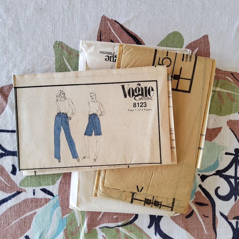 May include: A collection of vintage Vogue sewing patterns. The primary pattern features illustrations of a woman in pants and shorts. The pattern is labeled "Vogue Patterns 8123". The patterns are stacked on a floral patterned fabric.