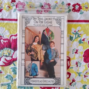 May include: A sewing pattern in a clear plastic bag. The pattern is for a jacket and features the text "Try This Jacket On For Sighs". The pattern shows images of the jacket worn in different styles. The brand name "Homestead Specialties" is at the bottom.