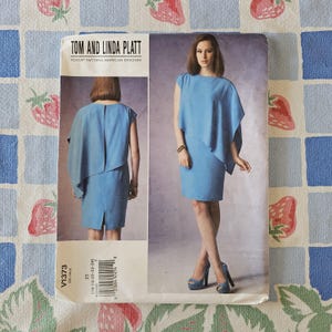 May include: A Vogue Patterns sewing pattern envelope for a Tom and Linda Platt design, labeled V1373. The front displays a light blue dress with an asymmetrical draped overlay, shown from both front and back views, with size range 16-18-20-22-24.