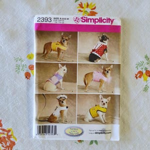 May include: Simplicity sewing pattern for dog clothes, size A XXS-M. The pattern features various outfits, including a yellow vest, a red polka-dot dress, and a pink top with a feather trim. The pattern includes the text "Designs for Truly Pets".