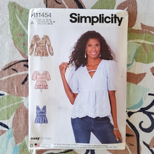 May include: A Simplicity sewing pattern, R11454, featuring a woman wearing a light blue top. The pattern includes illustrations of three different top designs. The text "easy-to-sew" is printed at the bottom of the pattern.