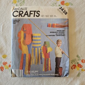 May include: A McCall's Crafts sewing pattern envelope 2438 titled Up Up and Away. The cover features illustrations of colorful fish-shaped wind socks and a child holding a long wooden pole. Text includes Learn to Sew for Fun and Focus on Overlock Sewing.
