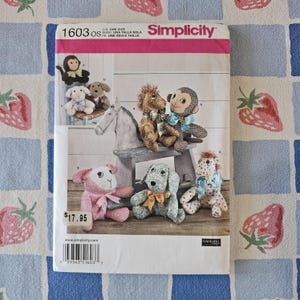 May include: A Simplicity 1603 sewing pattern envelope featuring illustrations of stuffed animals including a monkey, a horse, a lamb, and a dog. The envelope displays the text 1603 OS, Simplicity, and a price tag of $17.95 with a barcode at the bottom.