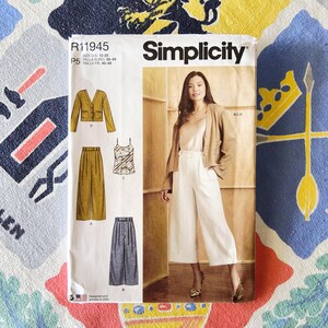 May include: A Simplicity sewing pattern envelope, R11945, featuring a woman in white pants and a tan jacket. The pattern includes illustrations of a jacket, pants, and a camisole. The text on the envelope reads "SIZE US 12-20" and "Designed and printed in USA."