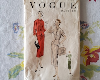 May include: Vintage Vogue sewing pattern for a dress, size 14, with a bust measurement of 32 inches and a hip measurement of 35 inches. The pattern features two illustrations of women wearing the dress, one in red and one in a striped pattern.