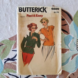 May include: Vintage Butterick sewing pattern 6889, featuring illustrations of two women wearing blouses. The pattern is labeled "Fast & Easy" and includes the size 8. The cover is aged with visible wear and tear.