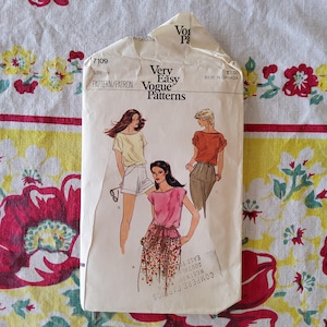 以下が含まれることがあります： ヴィンテージのVogue Patternsの縫製パターン封筒。封筒には、Tシャツとショートパンツ、ピンクのトップスと花柄スカート、オレンジのトップスとパンツなど、女性用衣料のデザインイラストが描かれています。封筒のテキストには「Very Easy Vogue Patterns」と書かれています。