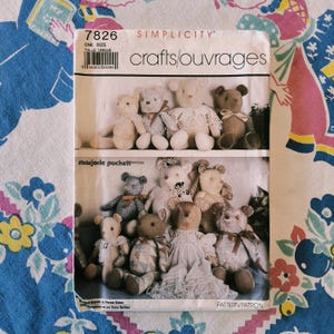 Puede incluir: Un sobre de patrón de costura Simplicity 7826 para manualidades con ilustraciones de varios osos de peluche. El frente muestra dos filas de osos de tela con diferentes colores, estampados y ropa, con el texto crafts/ouvrages y Marjorie Puckett.