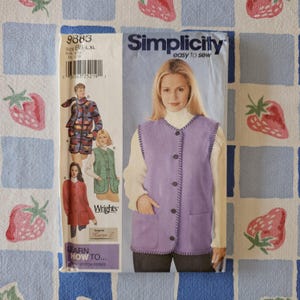 May include: A Simplicity 9883 sewing pattern envelope featuring a light purple button-front vest with whipstitch edges. The cover displays illustrations of three variations of the vest, including a patterned version and a solid red version.