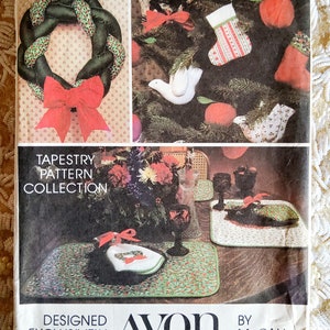 May include: A vintage Avon tapestry pattern collection featuring a green wreath with a red bow, a white dove, and a red and white stocking. The collection also includes placemats with a green and white floral pattern. The text "Designed Exclusively for Avon by McCall Patterns" is printed on the front of the package.