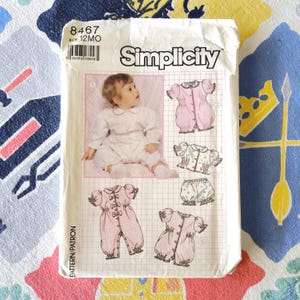 Op de afbeelding: Een vintage Simplicity naaipatroon voor babykleding, maat 12 maanden. De patroonhoes toont een baby in een witte outfit en illustraties van verschillende kledingontwerpen, waaronder een roze romper en een bloemen top.