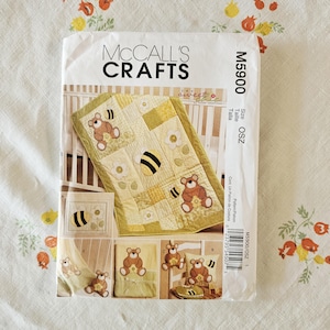 May include: A McCall's Crafts sewing pattern envelope, model M5900, featuring a yellow and green patchwork baby quilt with teddy bear and bee appliqués. The cover displays multiple project variations including a blanket, pillow, and bib.