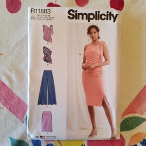 May include: Simplicity sewing pattern R11803, featuring a woman in a peach-colored dress with a side slit. The pattern includes designs for a top, pants, and a skirt. The size range is US 12-20, Euro 38-46, and French 40-48.