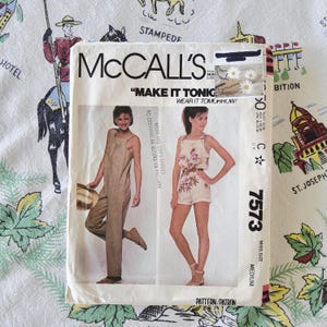 May include: A McCall's sewing pattern envelope, number 7573, featuring illustrations of a tan jumpsuit and a floral print romper. The text includes "MAKE IT TONIGHT, WEAR IT TOMORROW!" and "MISS SIZE MEDIUM." The white paper envelope shows two models.