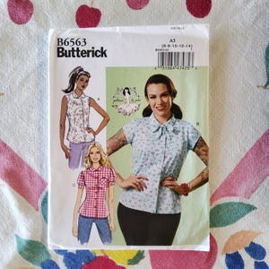 May include: Butterick B6563 sewing pattern for women's blouses. The pattern features illustrations of three blouse styles, including a floral print, a gingham print, and a solid color. The pattern size is A5 (6-8-10-12-14).