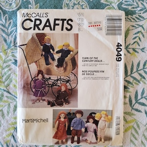 May include: A vintage sewing pattern for making turn of the century dolls. The pattern is from McCall's Crafts and features a doll in a wicker carriage, a doll in a purple dress, and a doll in a red dress. The pattern is titled "Turn of the Century Dolls" and "Nos Poupees Fin de Siecle".