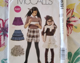Può includere: Un cartamodello per abbigliamento da ragazza, taglie 7-8, 10-12 e 14. Il cartamodello include istruzioni per realizzare un paio di pantaloncini a quadri, una gonna a balze e una gonna di jeans. Il cartamodello è etichettato come "Facile" e presenta il logo McCall's e il numero di cartamodello M6391.