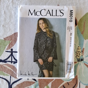 Könnte beinhalten: McCall's M8010 Schnittmuster mit einer Frau in einer schwarzen Jacke und einem Rock mit Sternmuster. Größen A5 (6-8-10-12-14) sind enthalten. Der Markenname und die Unterschrift des Designers sind sichtbar.