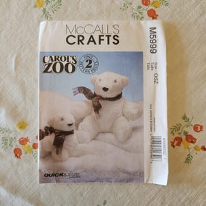 Può includere: Una busta per cartamodello McCall's Crafts M5999 per Carol's Zoo con due orsi di peluche bianchi che indossano sciarpe a quadri. La busta di carta bianca include il testo McCall's Crafts, Carol's Zoo, Only 2 Pattern Pieces e Quick & Easy.