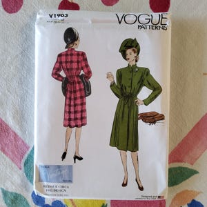May include: A vintage Vogue Patterns sewing pattern packet. The packet shows illustrations of two women's dresses. One dress is a red and black plaid, and the other is a green dress. The packet has the text "V1903" and "REISSUE CIRCA 1945 DESIGN".