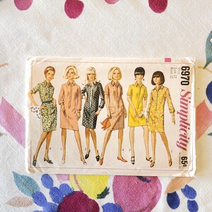 May include: Vintage Simplicity sewing pattern 6970 featuring illustrations of six women in shirt dresses. The pattern includes a size 12, bust 32. The cover has a retro design with a price of 65¢.