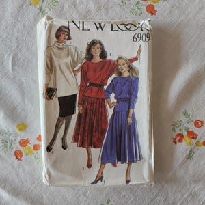 May include: A New Look 6909 sewing pattern envelope featuring illustrations of three outfits. One figure wears a cream turtleneck with a black skirt, another a red top with a patterned skirt, and the third a blue top with a pleated skirt.