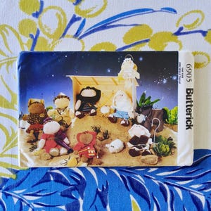 May include: A Butterick pattern envelope featuring a nativity scene with plush toy figures. The scene includes a stable, donkey, and various characters in a starry night setting. The envelope is labeled "6905" and "ONE SIZE UNE SEULE TAILLE".