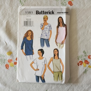 May include: A Butterick 3383 Fast & Easy sewing pattern envelope featuring illustrations of five different top styles. The designs include various necklines, sleeve lengths, and a pocket detail, with size range XS, S, M printed on the white paper packaging.