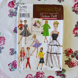 Puede incluir: Un patrón de costura vintage de Simplicity Fashion Doll, con ilustraciones de diseños de ropa para muñecas. El paquete incluye el número 5785 y el texto "ONE SIZE". La portada muestra varios conjuntos de muñecas en diferentes estilos.