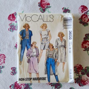 May include: A vintage McCall's sewing pattern envelope featuring illustrations of women's clothing designs. The designs include a skirt suit, pants suit, shorts set, and a long shirt dress. The envelope is cream-colored with the text "NON-STOP WARDROBE".