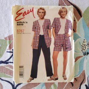 May include: An Easy stitch 'n save sewing pattern packet. The packet features a woman wearing a red, white, and blue plaid jacket and either matching shorts or navy blue pants. The packet has the number 8767 and the words "Easy stitch 'n save".