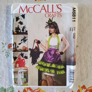 May include: A sewing pattern for a Halloween costume featuring a black and green dress with a purple satin skirt and a black and white witch hat. The pattern is from McCall's Crafts and is size OSZ. The pattern includes instructions for making a witch costume.