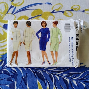 May include: A Butterick sewing pattern package featuring illustrations of four different dress designs. The package includes the text "Your Personal Fitting Pattern" and the number "6092". The background is a blue and yellow floral pattern.
