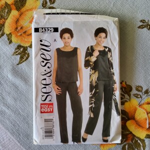 May include: A vintage See & Sew sewing pattern packet, featuring a woman modeling a black sleeveless top, pants, and a long jacket with a floral design. The packet has the text "YES! it's easy" and pattern number B4329.