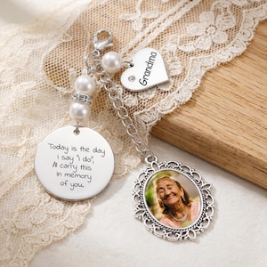 Könnte beinhalten: Ein silberner Charm mit einem Foto einer lächelnden Frau, einem herzförmigen Charm mit dem Wort "Oma" und einem runden Charm mit dem Text "Heute ist der Tag, an dem ich 'Ja' sage, ich werde dies in Erinnerung an dich tragen."