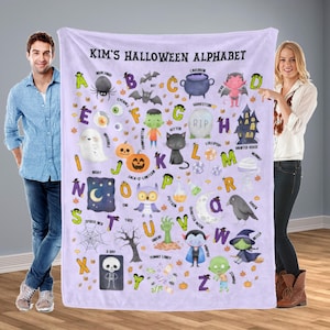 Pode incluir: Um cobertor lilás com tema de Halloween com um alfabeto e ilustrações assustadoras. O cobertor inclui imagens de um fantasma, abóbora, gato e bruxa. O texto no cobertor diz "Kim's Halloween Alphabet".