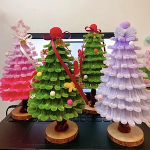 Puede incluir: Cuatro árboles de Navidad en miniatura hechos de limpiapipas. Los árboles están decorados con pompones, cuentas y cinta. Los árboles están sobre bases de madera.