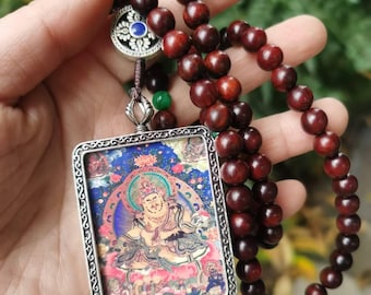 May include: A wooden bead necklace with a rectangular pendant featuring a colorful religious image. The pendant has a silver-colored frame. The beads are a deep reddish-brown color.