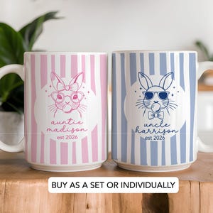 May include: Two ceramic mugs with white handles. One mug is pink and white striped with a bunny design and the text "Auntie Madison est 2026". The other mug is blue and white striped with a bunny design and the text "Uncle Harrison est 2026".