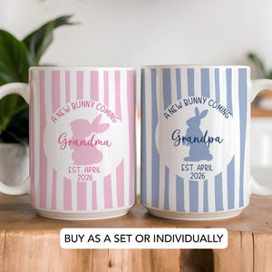 May include: Two white ceramic mugs with vertical striped patterns. One mug is pink and white, the other is blue and white. Each mug has a bunny graphic and the text "A New Bunny Coming" and "Grandma" or "Grandpa".
