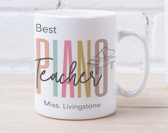 Może przedstawiać: Biały ceramiczny kubek z napisem "Best Piano Teacher" w kolorowych blokowych literach i czcionce. Obok słowa "Piano" znajduje się rysunek fortepianu. Poniżej wydrukowano imię i nazwisko "Miss. Livingstone".