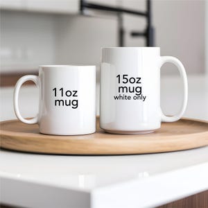 Pu&ograve; includere: Due tazze in ceramica bianca di diverse dimensioni, ciascuna con un'etichetta stampata in nero. La tazza pi&ugrave; piccola recita "11oz mug", mentre la pi&ugrave; grande recita "15oz mug white only". Le tazze sono esposte su un vassoio di legno.