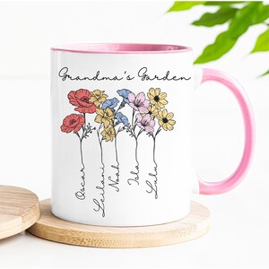 Pu&ograve; includere: Tazza in ceramica bianca con interno e manico rosa. La tazza presenta un design floreale con le parole "Grandma's Garden" e nomi sotto i fiori. I fiori sono rossi, gialli, blu e rosa.