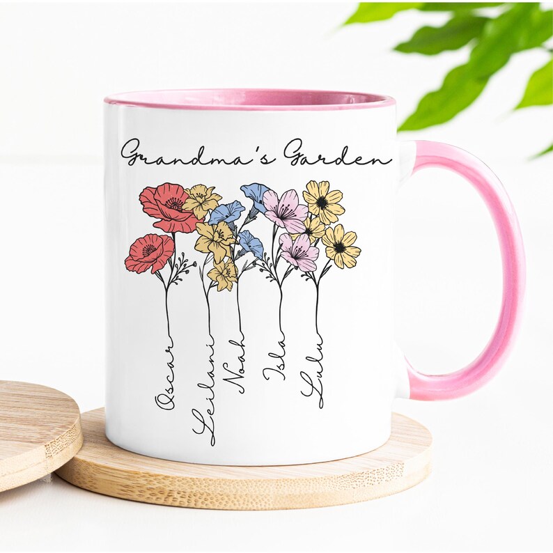 Pu&ograve; includere: Tazza in ceramica bianca con interno e manico rosa. La tazza presenta un design floreale con le parole "Grandma's Garden" e nomi sotto i fiori. I fiori sono rossi, gialli, blu e rosa.