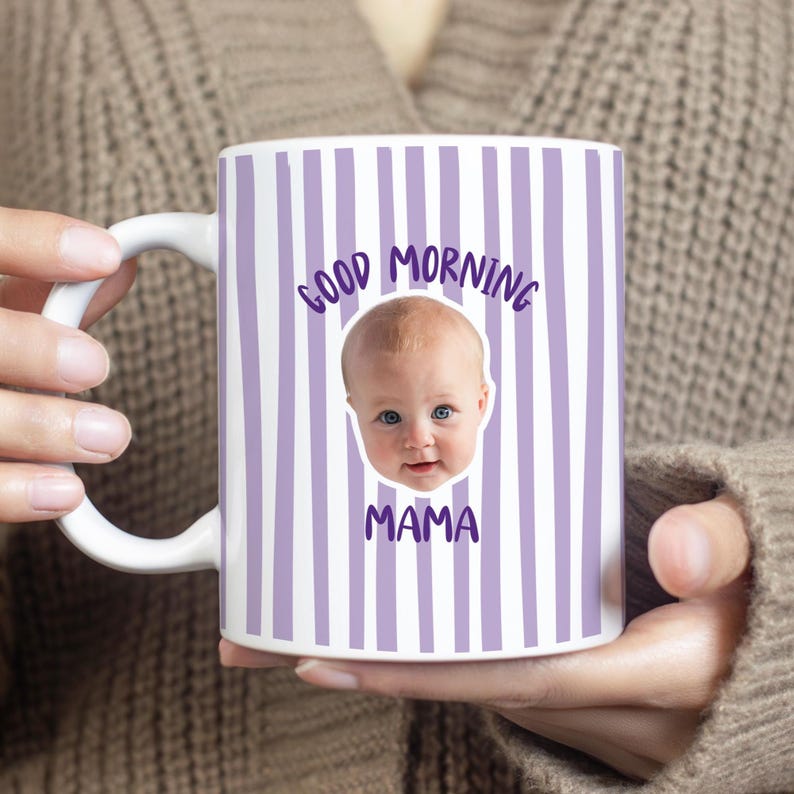 May include: A white ceramic mug featuring vertical lavender stripes and a central photographic print of a baby's face. The text "GOOD MORNING" is printed in purple above the baby's face, and the word "MAMA" is printed in purple below it.
