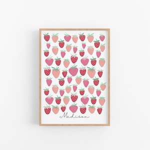 Op de afbeelding: Een ingelijst print met een witte achtergrond en een patroon van roze en rode aardbeien. De naam "Madison" staat in cursief onderaan de print.