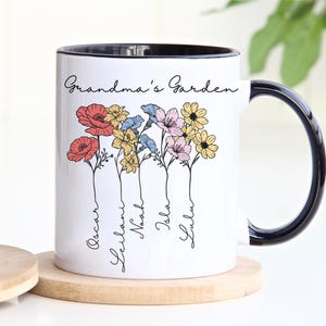 Pu&ograve; includere: Tazza in ceramica bianca con bordo e manico neri, con un design floreale con fiori rossi, gialli, blu e rosa. Le parole "Grandma's Garden" sono scritte sopra i fiori, con nomi sotto.