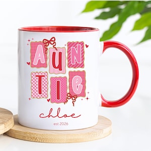 May include: White ceramic mug with a red interior and handle. The mug features the word "AUNTIE" in pink and red letters, with the name "chloe" and the year "est 2026" in red script. The design includes hearts and bows.